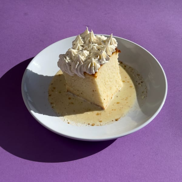 Slice of tres leches cake with whipped cream and a creamy sauce on a white plate.