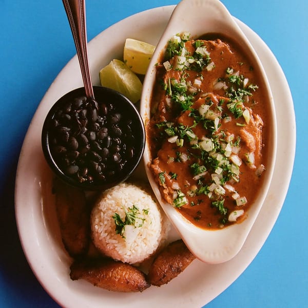 Cuban dish with meat in red sauce, white rice, black beans, plantains, and lime wedges.