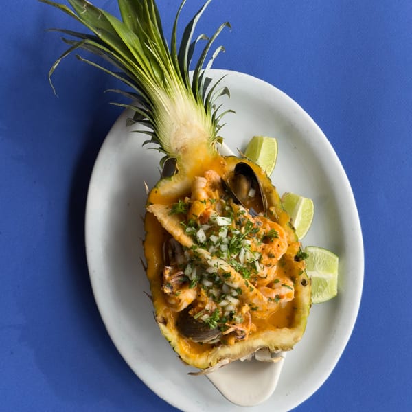 Cuban seafood dish with shrimp, mussels, and fish, served in a pineapple half with lime wedges.