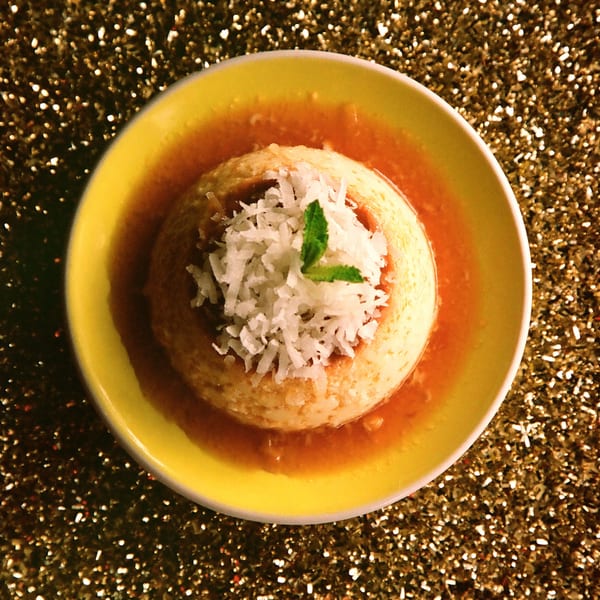 Cuban flan dessert with caramel sauce, topped with shredded coconut and a mint leaf.