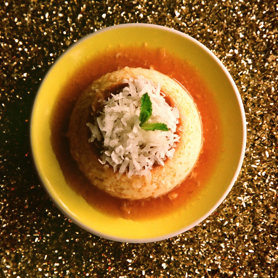 Cuban flan dessert with caramel sauce, topped with shredded coconut and a mint leaf.