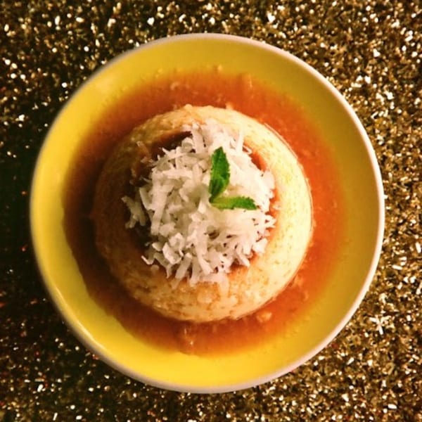 Cuban flan dessert with caramel sauce, topped with shredded coconut and a mint leaf.