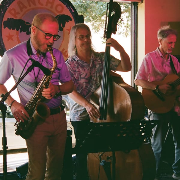 Three musicians performing live music with a saxophone, upright bass, and guitar at Rancho Alegre.