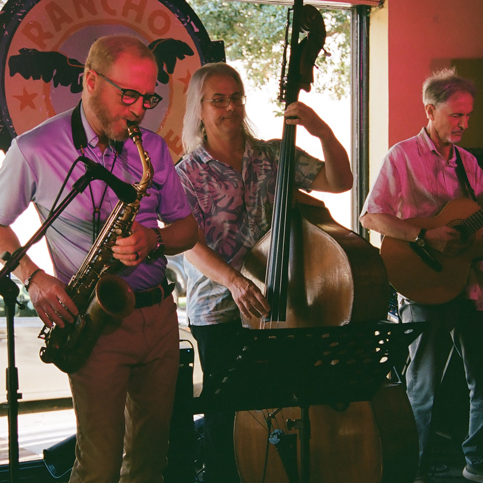 Three musicians performing live music with a saxophone, upright bass, and guitar at Rancho Alegre.
