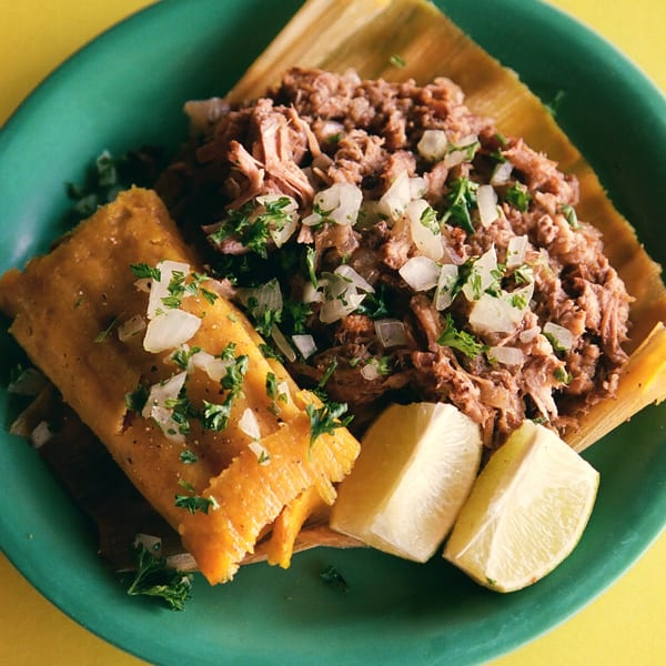 Cuban tamale and shredded pork with onions, cilantro, and lime wedges on a green plate.